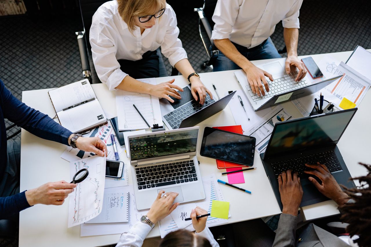 home-hero-bg Overhead view of a corporate team collaborating with laptops and documents.